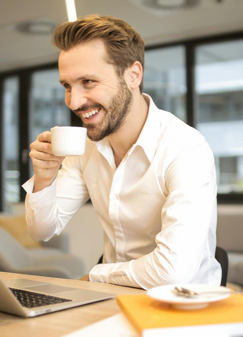 A man drinking coffee in front of his laptop